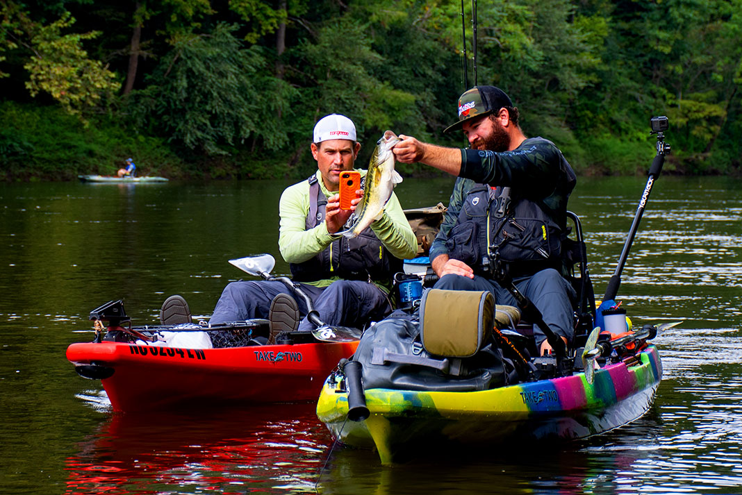 one man photographs a bass caught by another from Jackson tandem kayaks
