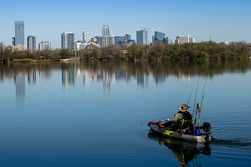 kayak angler paddles on still water in front of a cityscape