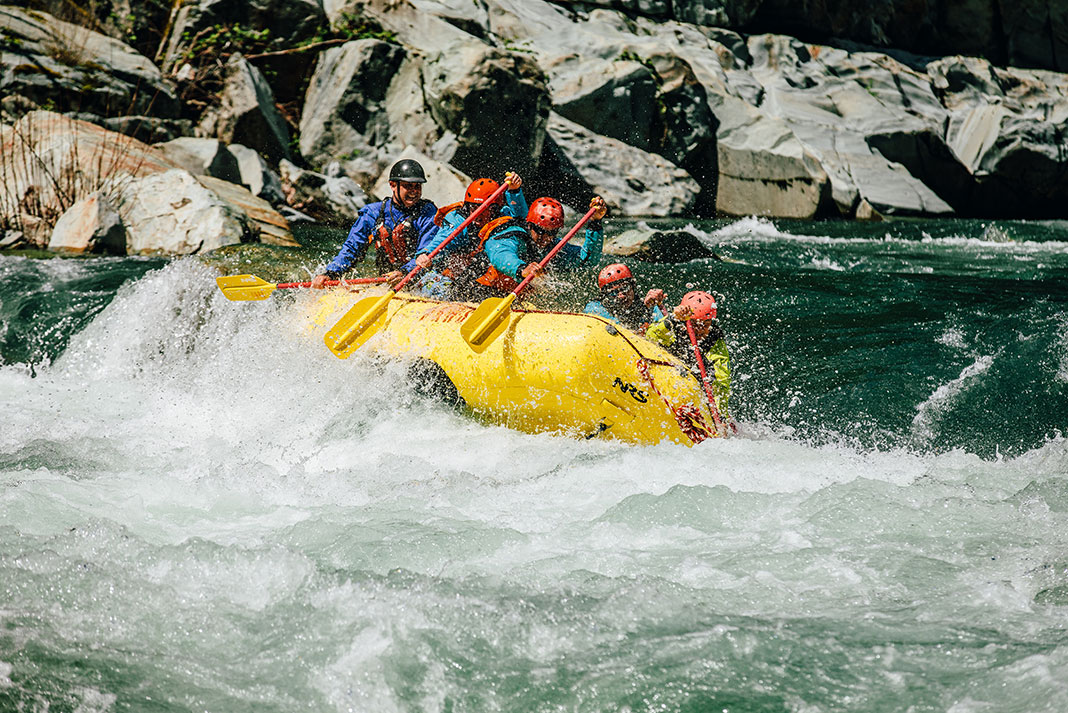 a group of people paddle a yellow whitewater raft through rapids