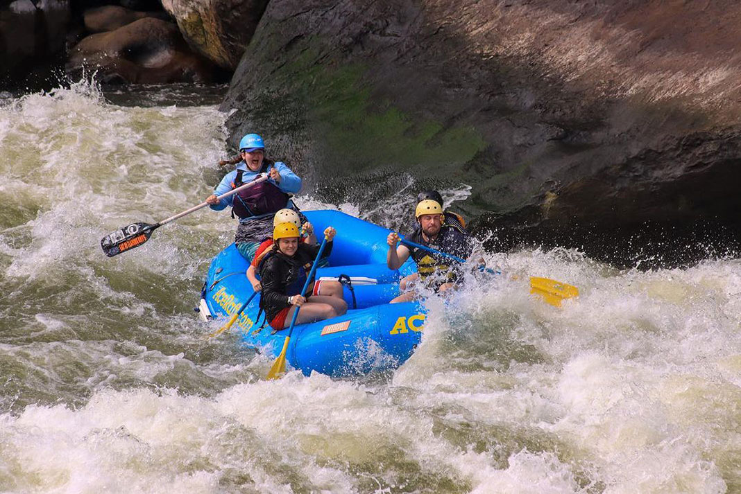 Ash Manning and three other people paddle a whitewater raft through rapids