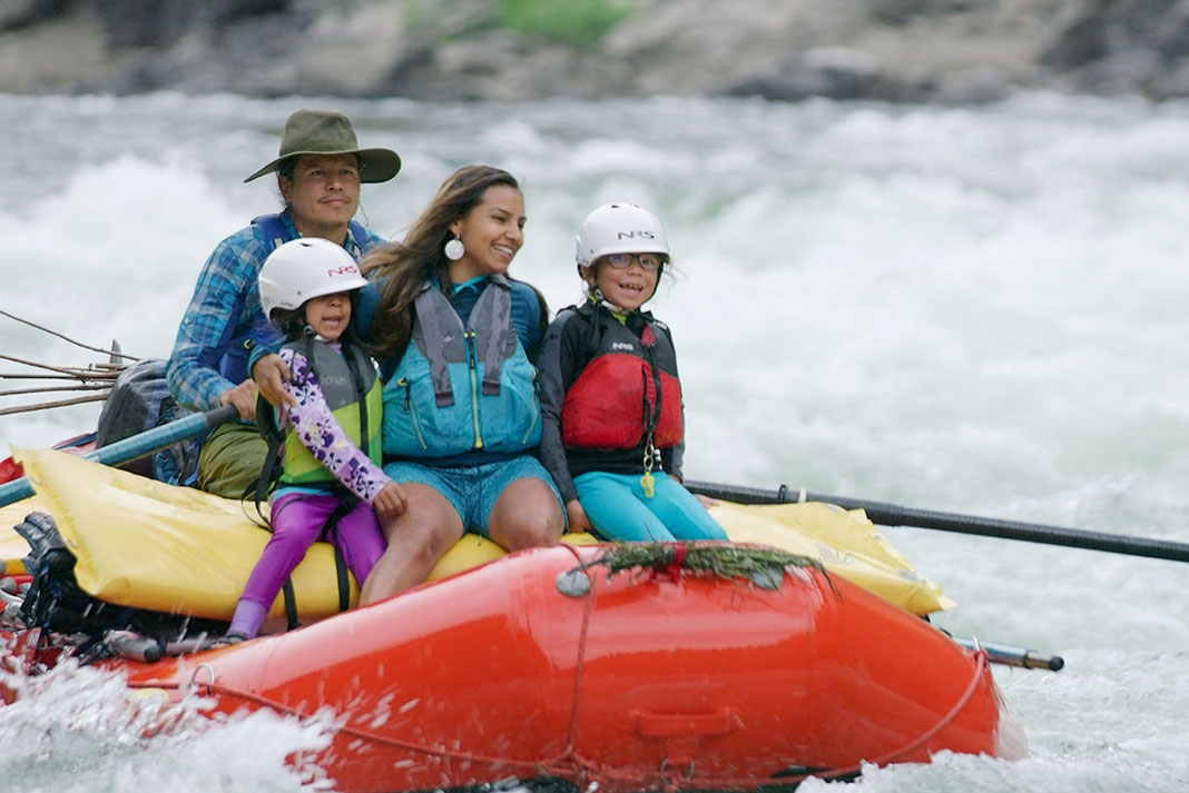 a hapy Indigenous family rides on a whitewater raft