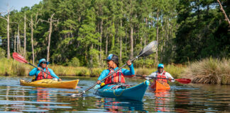 three Black men and women kayaking on calm water