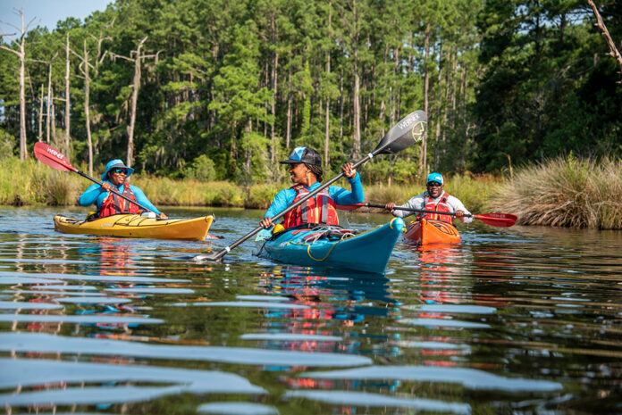 three Black men and women kayaking on calm water