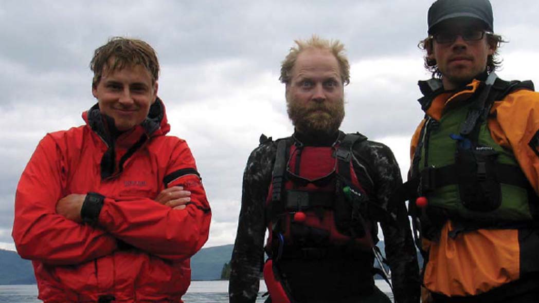 Three male expedition sea kayakers pose for the camera in Puffin Cove during their circuit of Haida Gwaii by kayak