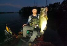 kayak angler holds up a largemouth bass caught while fishing at night
