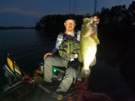 kayak angler holds up a largemouth bass caught while fishing at night