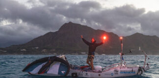Man stands with flare on top of custom-built expedition paddleboard ready for major feats of paddling