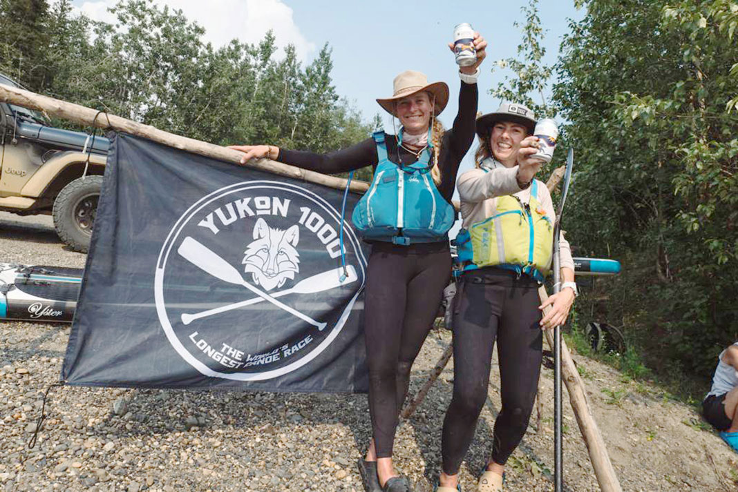 two woman paddleboarders stand in front of a Yukon 1000 banner