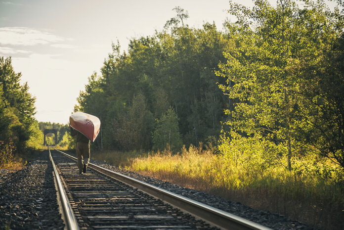 person portaging a canoe along train tracks in the sunlight