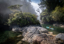 a person kayaking through a rocky, lush wilderness scene