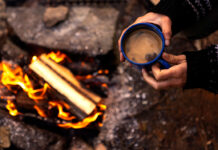 overhead photo of a person holding a mug of coffee over a campfire