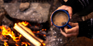overhead photo of a person holding a mug of coffee over a campfire