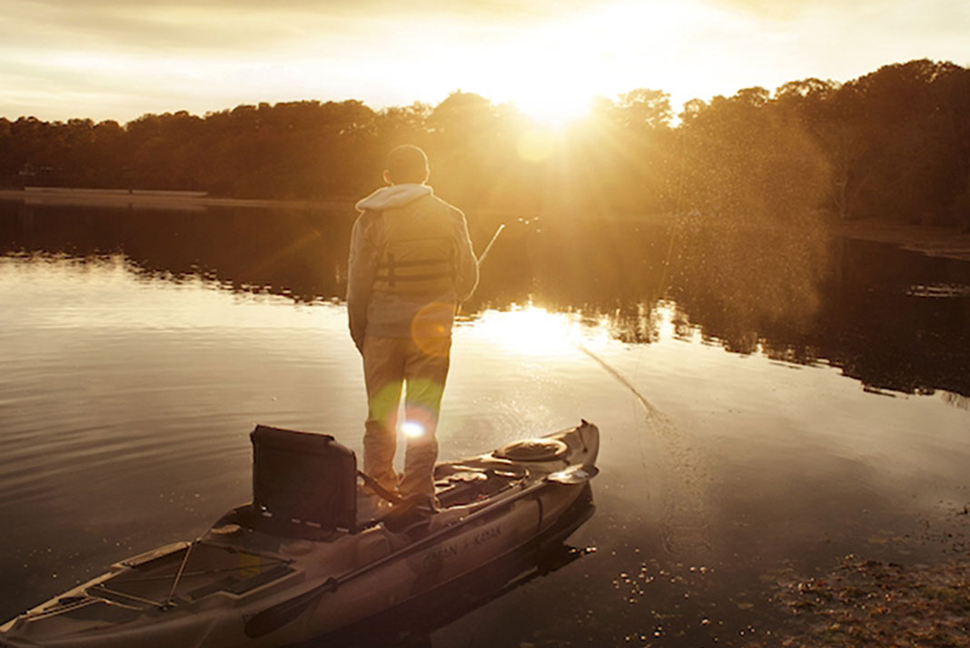 man stands up on a kayak and fishes in the morning light