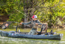 man uses landing net to catch large bass from a kayak, demonstrating kayak fishing mastery