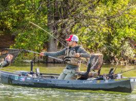 man uses landing net to catch large bass from a kayak, demonstrating kayak fishing mastery