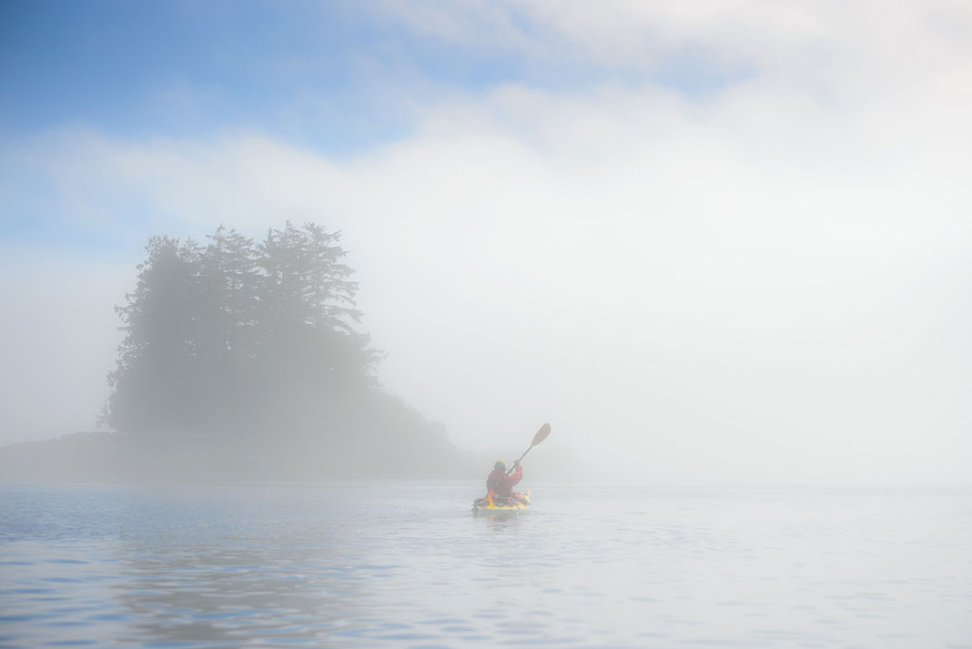 sea kayaker paddles in fog in front of small island