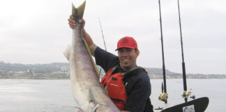 kayak angler holds up large fish caught with fishing accessories