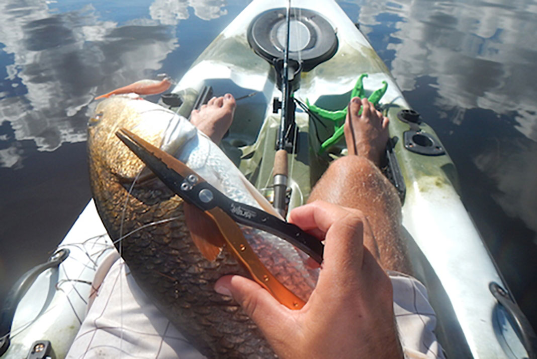 kayak angler uses pliers to unhook his catch, an essential fishing accessory