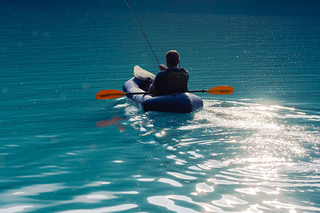 person fishes from an inflatable paddle kayak