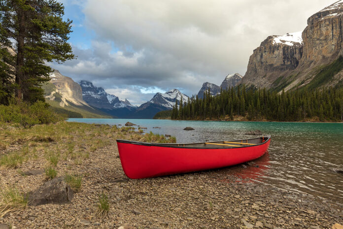 red canoe sits on riverbank in front of mountains