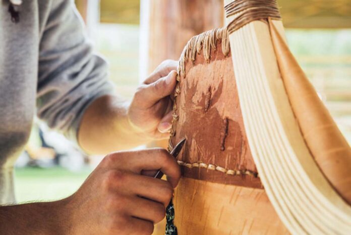 A student uses bark etching (scrafitto) to add a moose to the canoe