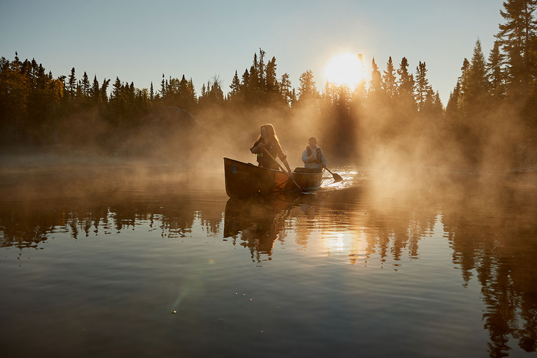 Couple paddling canoe on misty lake.