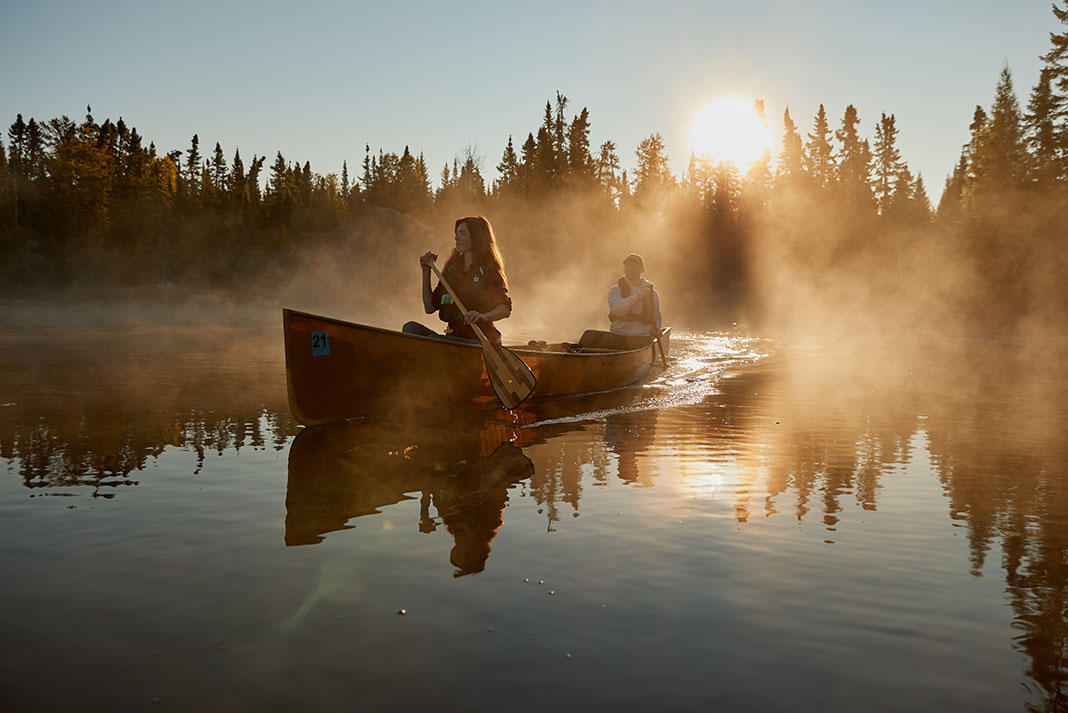 pair of canoeist paddle through morning mist in Minnesota's Boundary Waters Canoe Area