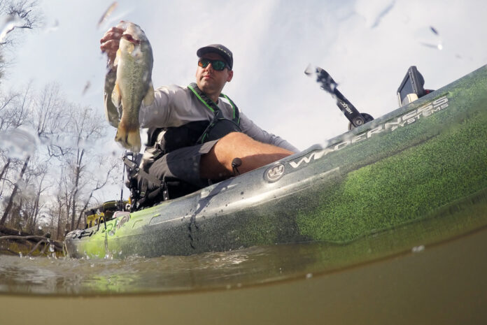 Low angle of man sitting on sit-on-top fishing kayak and lifting a fish out of the water.