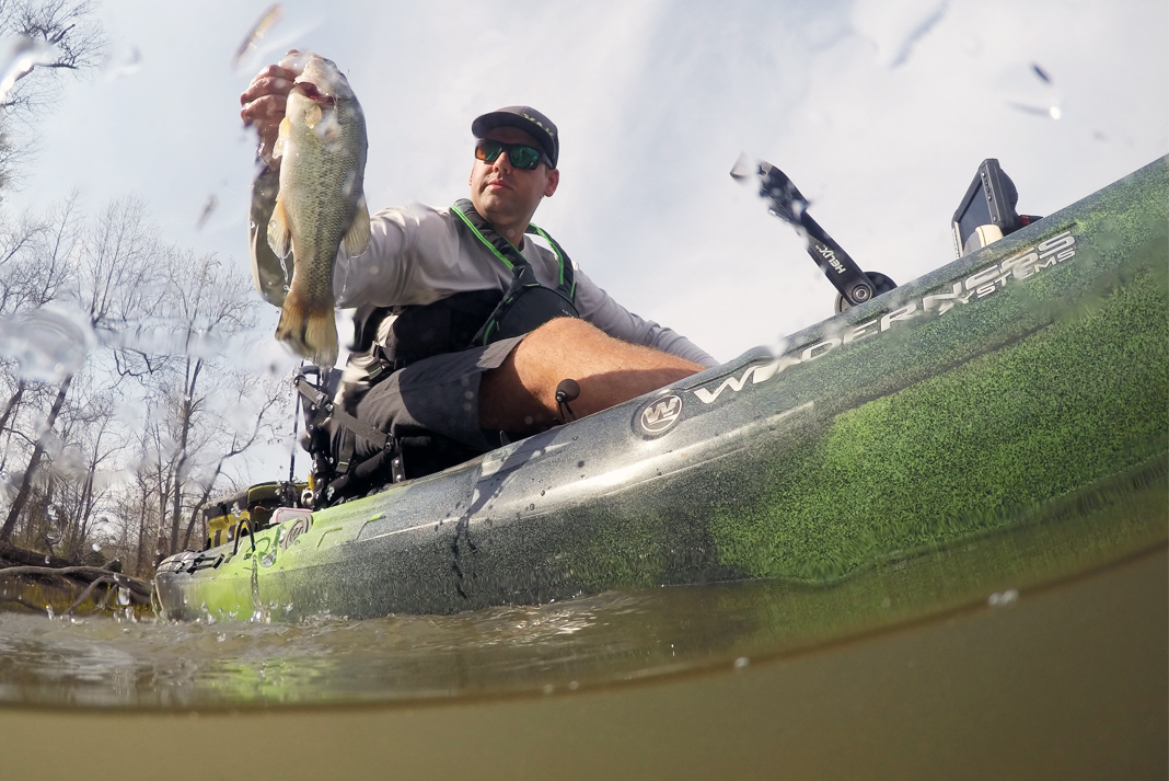 Low angle of man sitting on sit-on-top fishing kayak and lifting a fish out of the water.