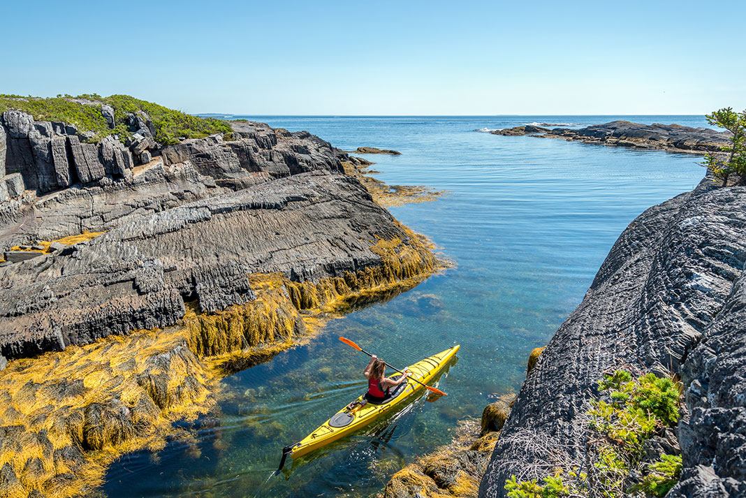 Woman paddling sea kayak on narrow passage between rocky shores