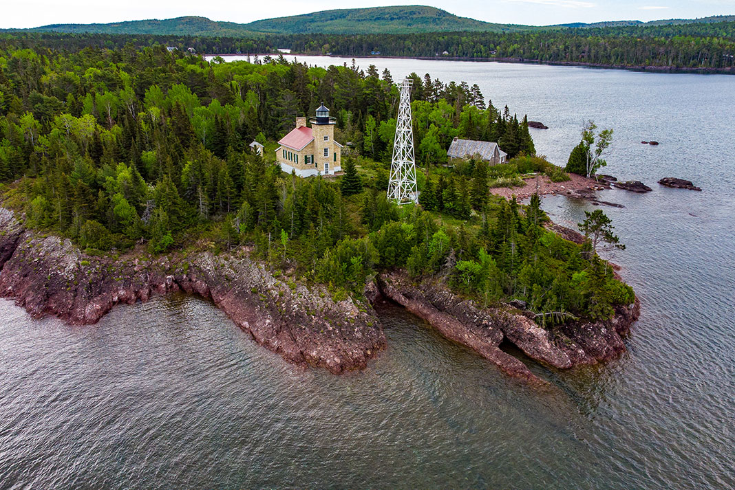 Lighthouse sits on edge of rocky peninsula.