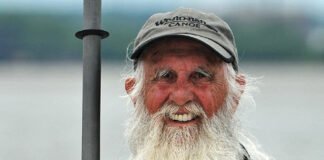 80-year-old “Grey Beard Adventurer” Dale Sanders stands smiling while holding a paddle