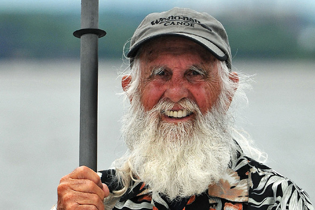 80-year-old “Grey Beard Adventurer” Dale Sanders stands smiling while holding a paddle