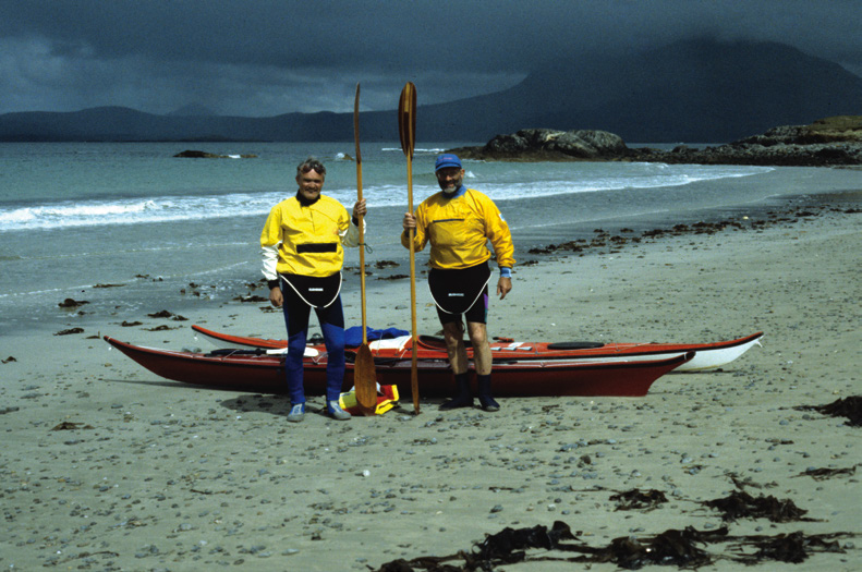 two men pose with paddles on the beach in front of their sea kayaks on an island off the west coast of Ireland