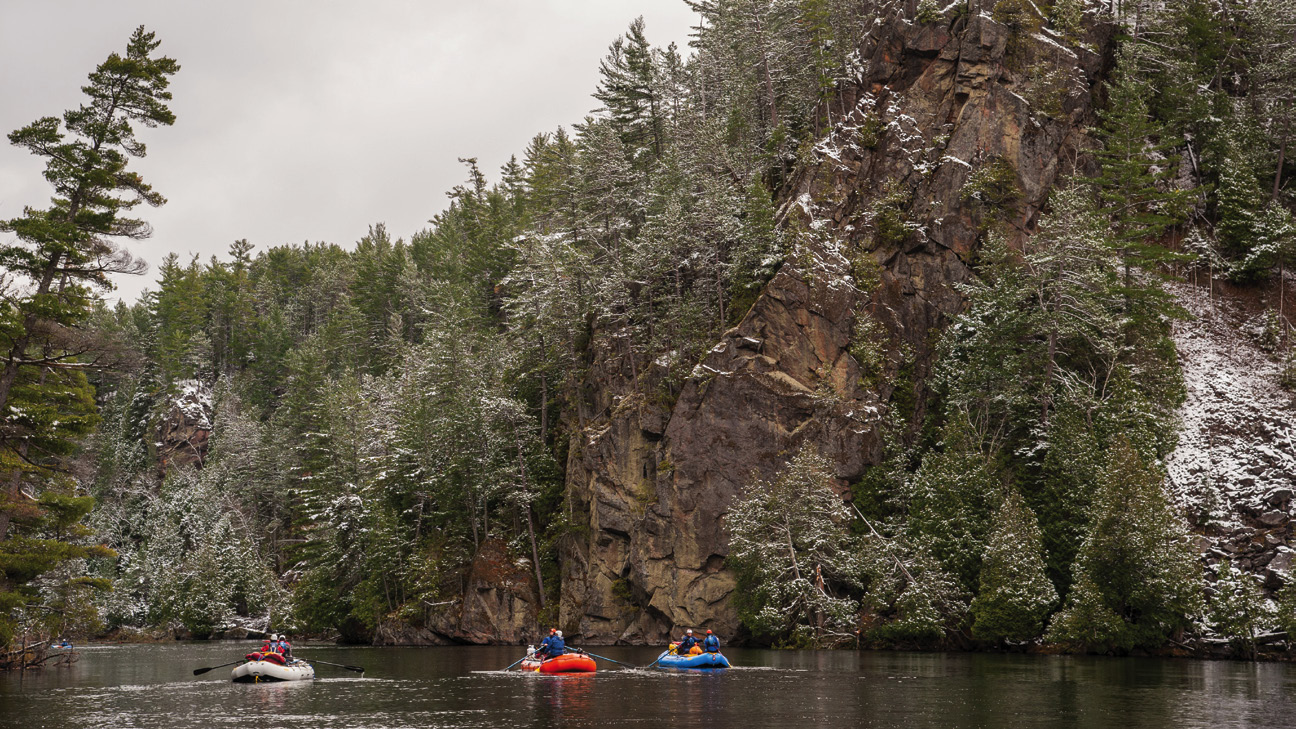 students paddle rafts past a snowy rocky outcrop
