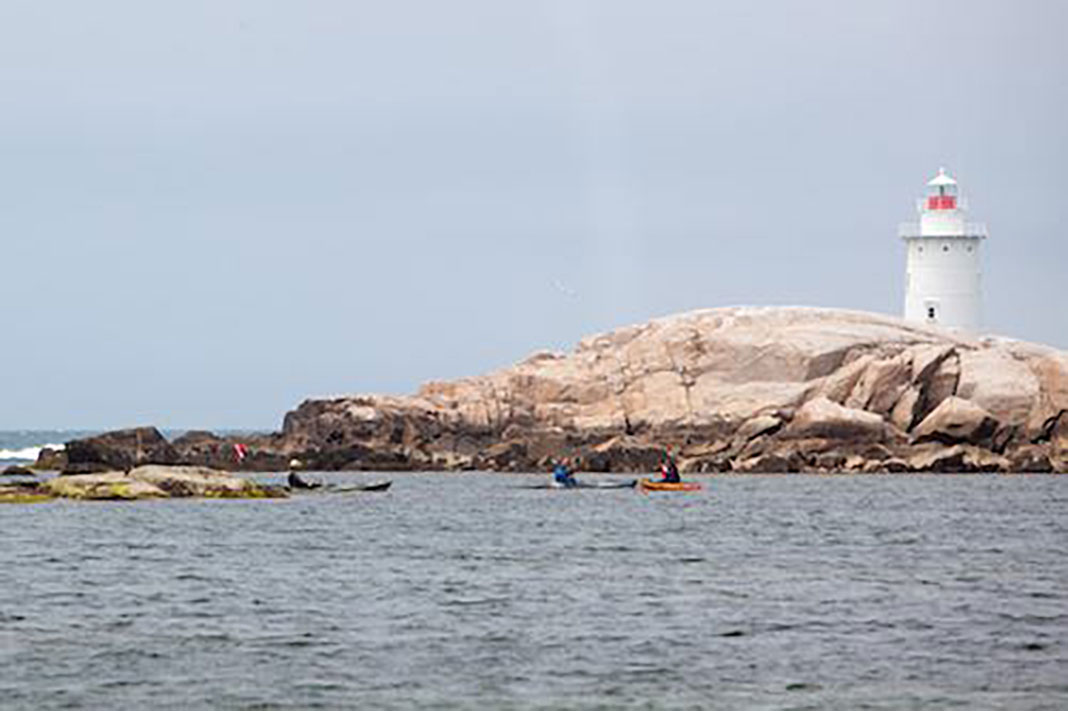 kayak anglers paddle in front of a lighthouse on a rocky outcrop