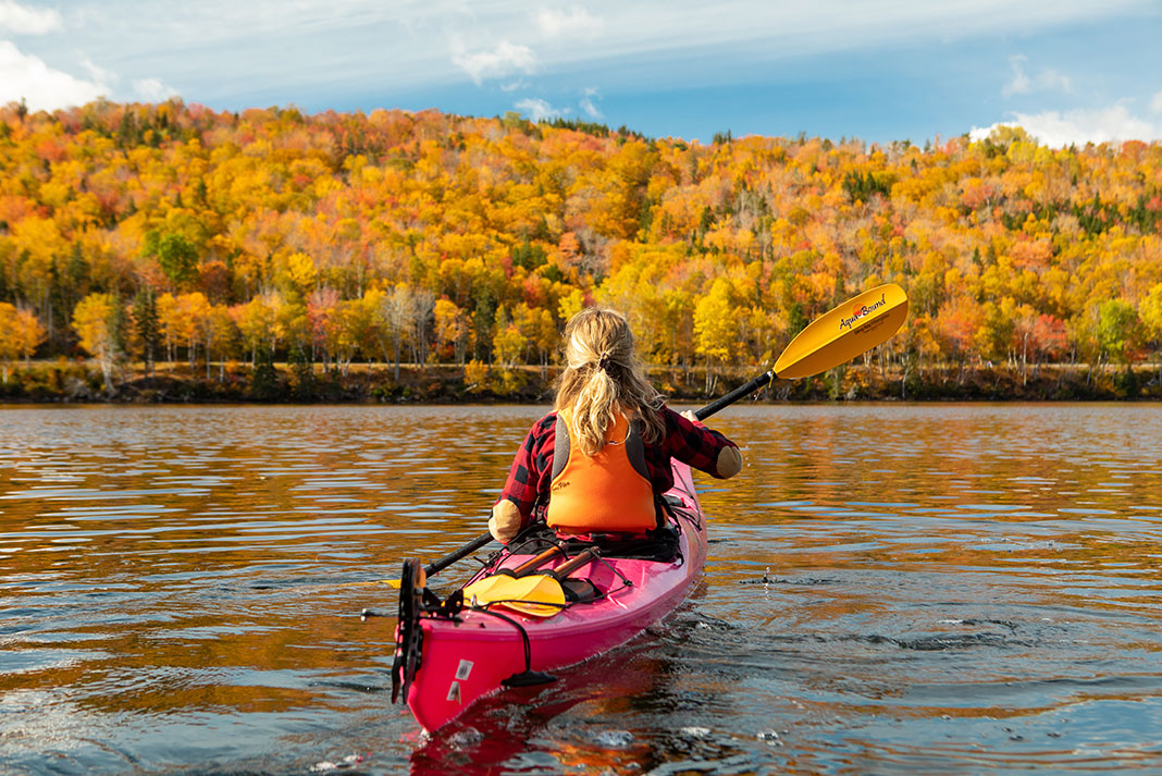 Woman paddling sea kayak with golden leaves in the background.