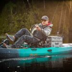 Best Pedal Fishing Kayaks For 2026 Side view of angler in blue sit on top fishing kayak.