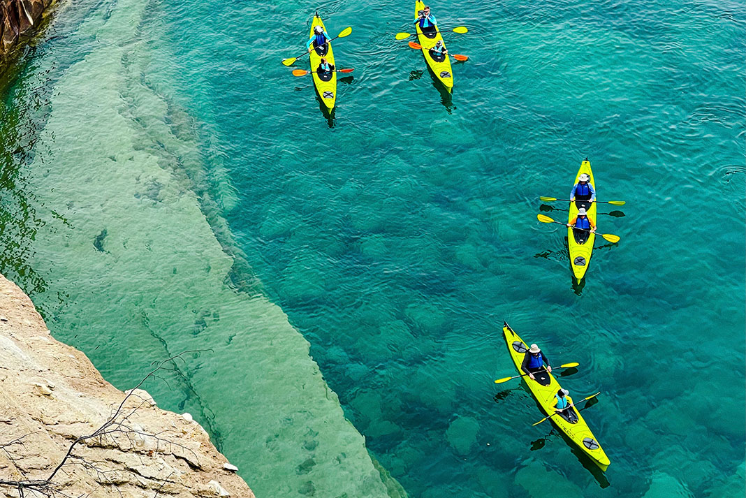 Overhead shot of yellow tandem kayaks being paddled on clear, blue waters.