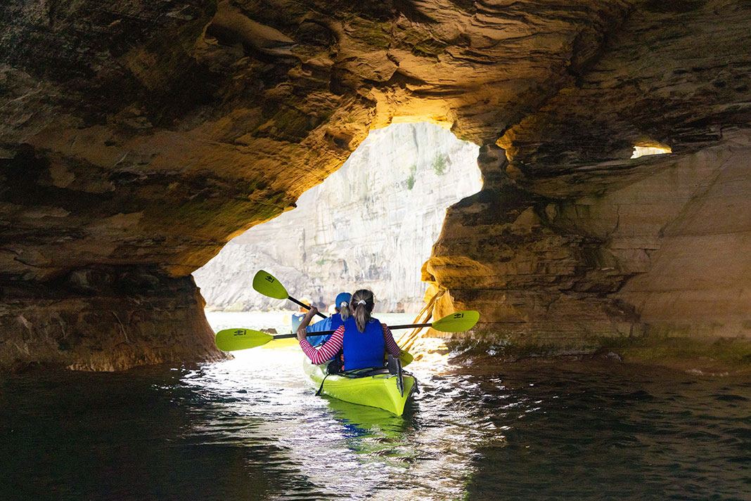Two women paddling a tandem kayak through a sea cave.