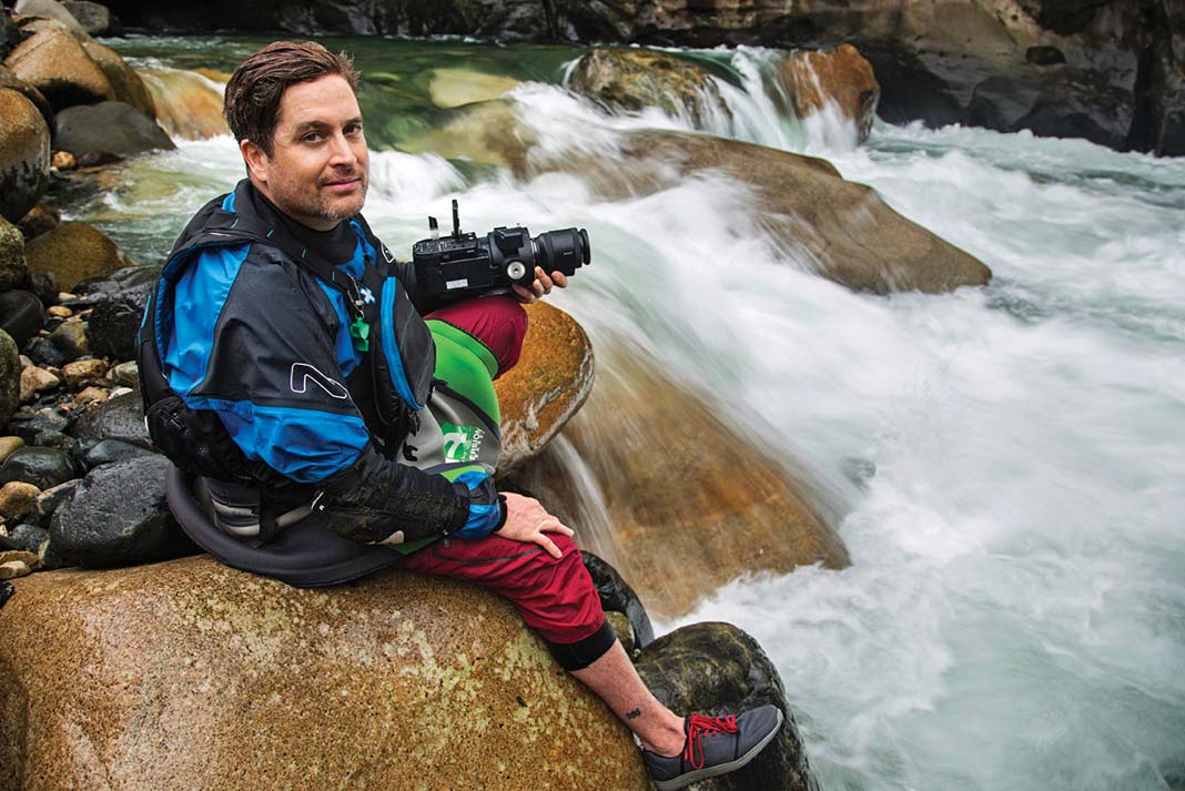 Paddling filmmaker Mike McKay poses with camera beside a set of rapids after quitting his day job