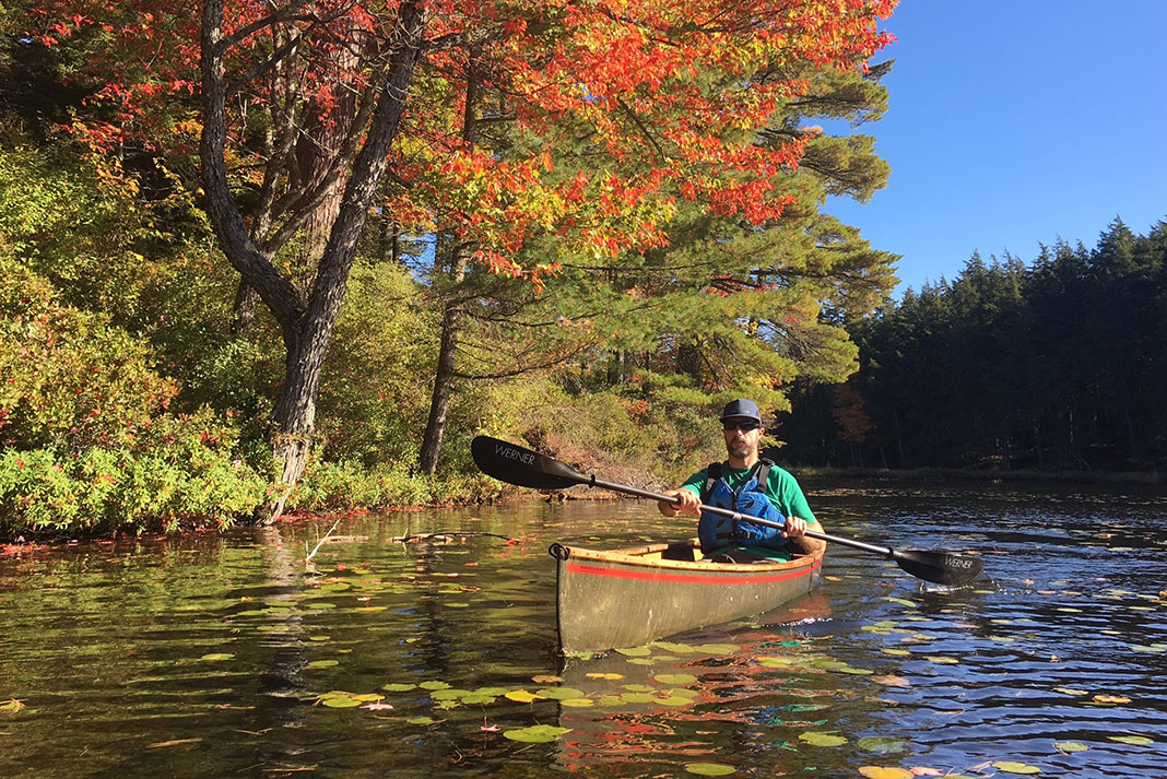 Man paddling canoe with double bladed paddle in the fall.