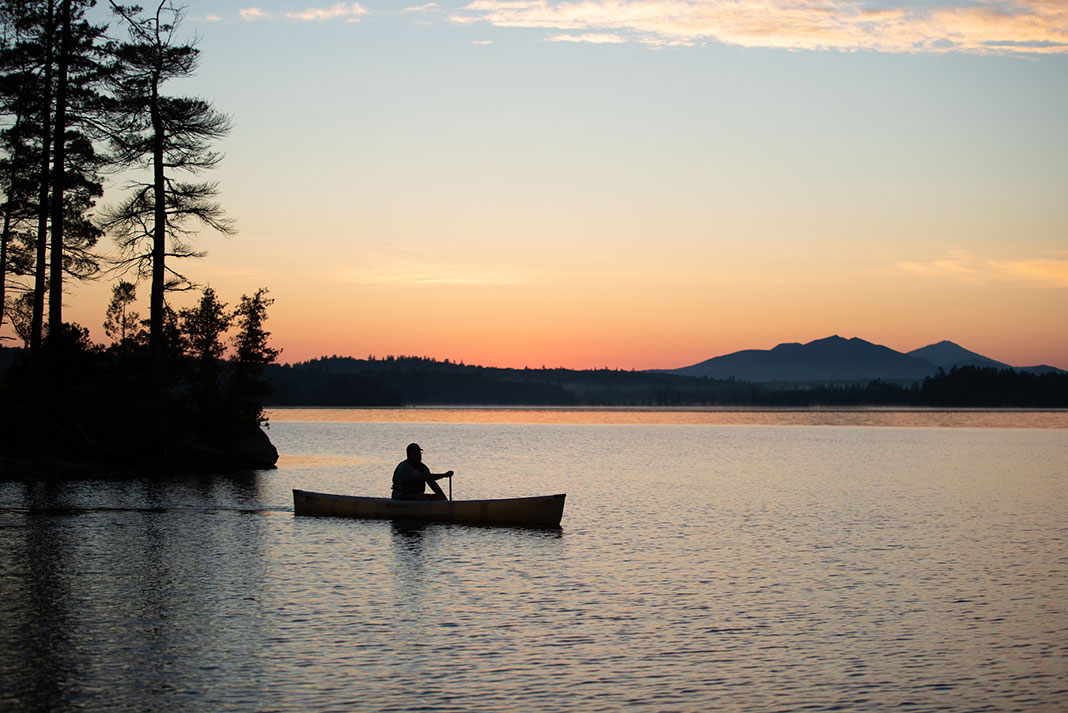 Silhouette of man paddling a canoe at sunset.