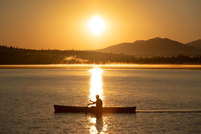 Person paddling a canoe solo as the sun goes down.