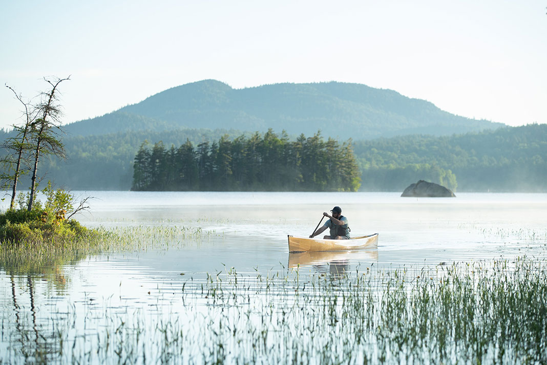 man paddles canoe on Middle Saranac Lake at dawn