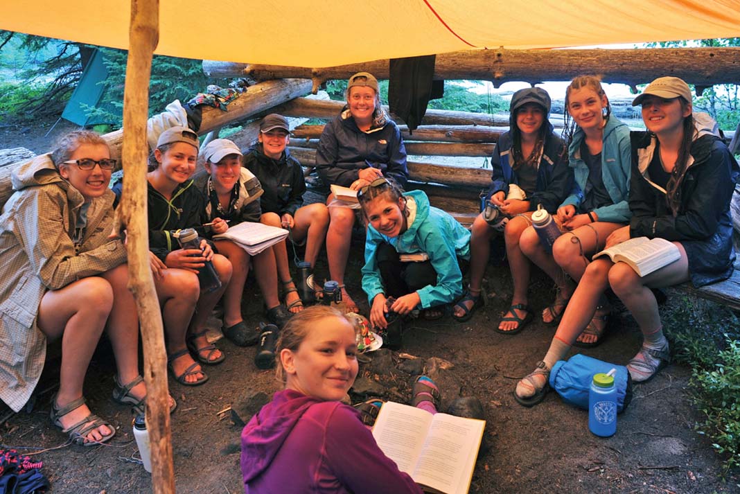 a group of young women learning to be paddling guides gathered under a tarp
