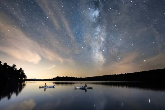 a photo of two kayakers floating on still water under the starry night sky