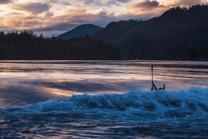 a person whitewater kayaking in a set of rapids on a river at dusk