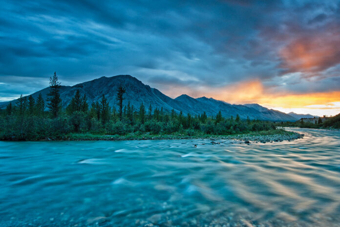 mountains and swift-flowing river under a cloudy dusk sky