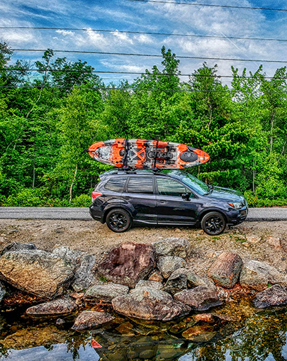 Vibe kayak on top of SUV parked at side of the road.
